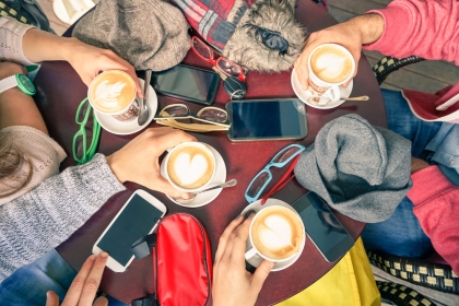 Taken from above, students sit around table with coffees, mobile phones and books